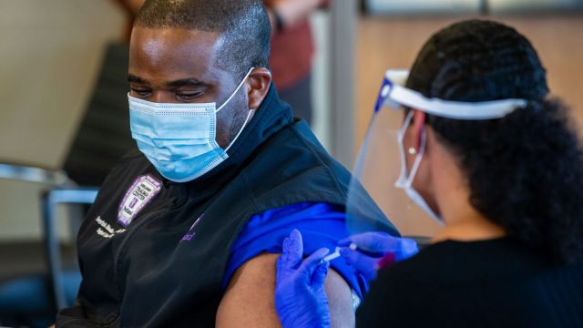 COVID單位護士Tonychris「 TC」 Nnaka，（左）在12月15日在Parkland醫院舉行的媒體活動中，從職業健康總監Stephanie Collins那裡接受了輝瑞的COVID-19疫苗接種。