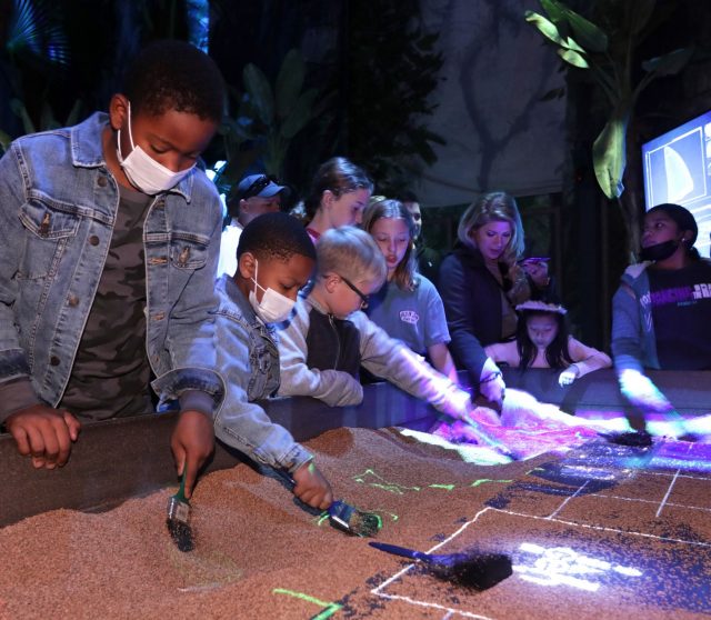 游客们在“侏罗纪世界：展览”中刷沙子寻找化石，在 The Colony 的 Grandscape。 该展览基于电影专营权。